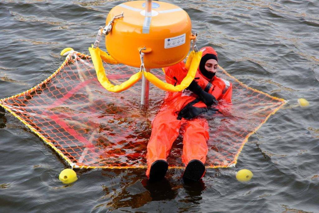 Person in a survival suit laying inside a RescueStar Basket in the water.