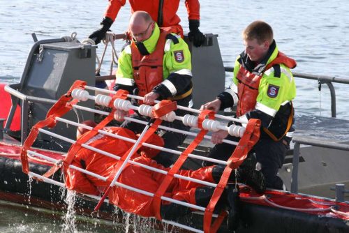 Two people pulling a person from the water laying in a rescue frame
