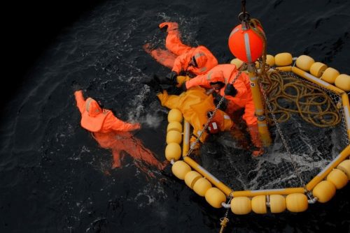 Dacon Rescue Basket laying in the water with people in and around it. One person being dragged inboard by another.