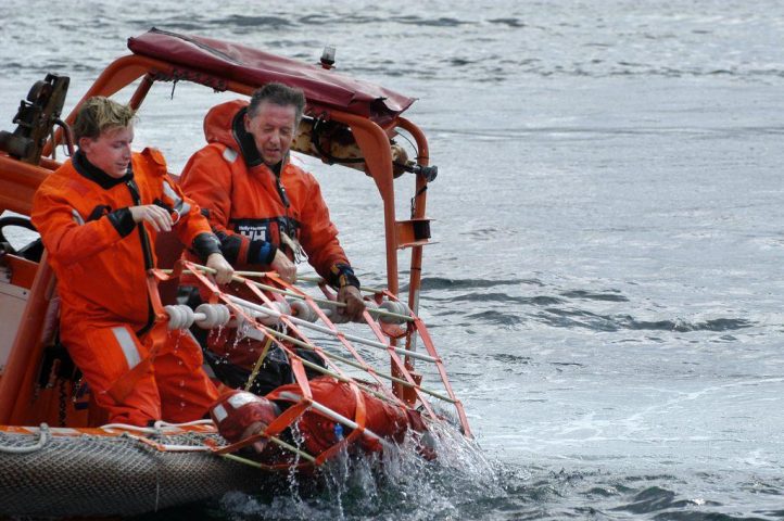 Horizontal recovery of man overboard being hauled out of the water in a rescue net.